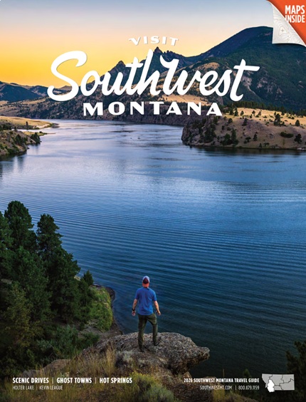 Traveler stands on rocky cliff overlooking a blue lake at sunrise, with pine trees and mountains in the distance; 'Visit Southwest Montana' overlay text.